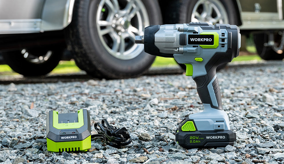Cordless impact wrench with battery and charger on gravel beside a vehicle, showing a green and gray Workpro design