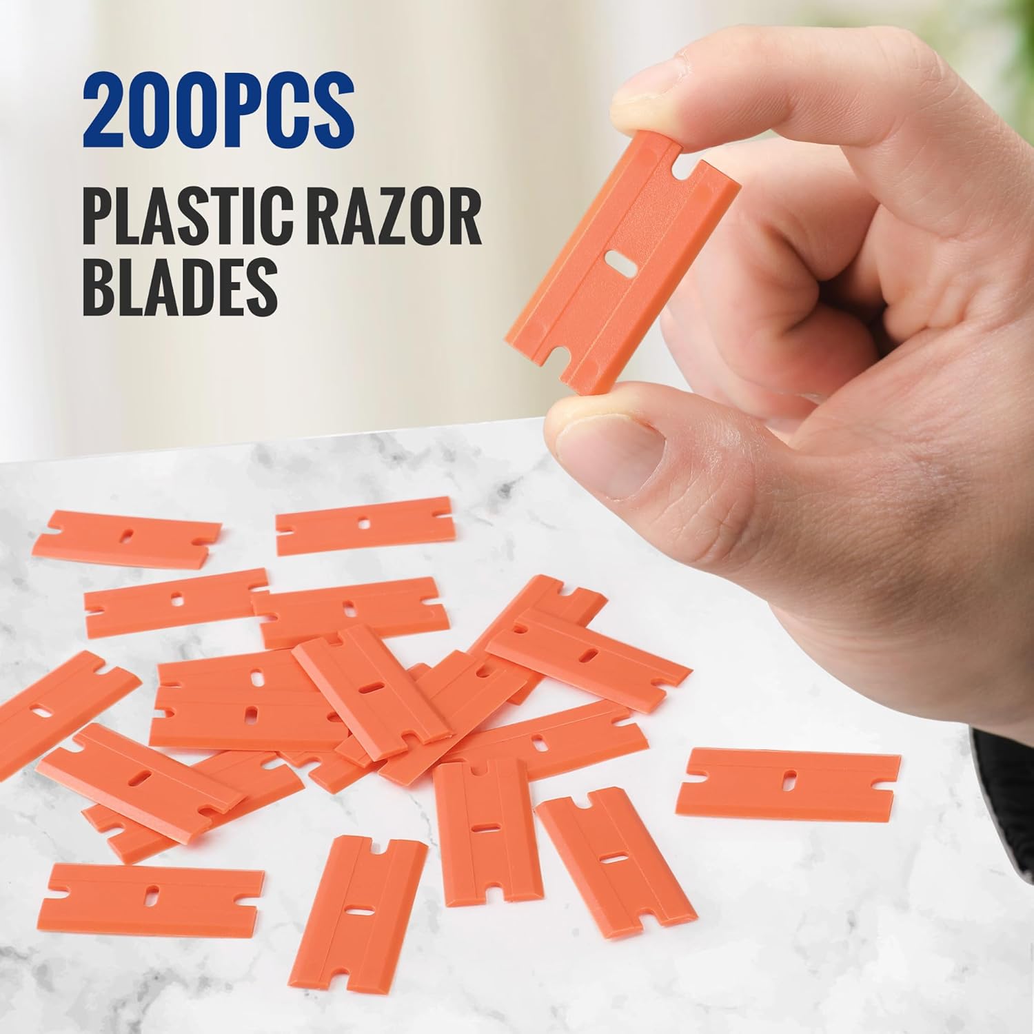 Orange plastic razor scraper blades, 200-count refill set, held above a pile