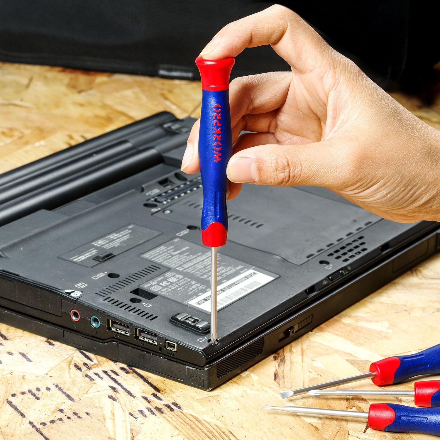 Hand holding blue-and-red screwdriver with silver shaft on electronic device