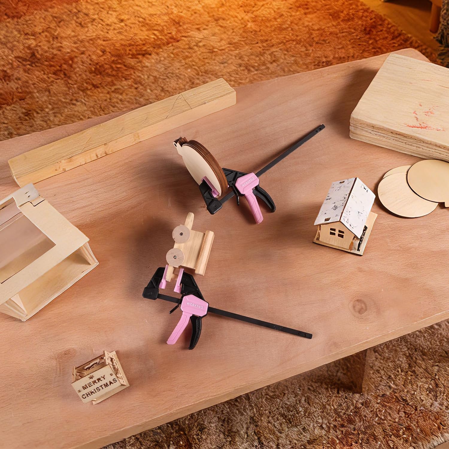 Set of pink mini bar clamps on a plywood work surface securing multiple wood parts