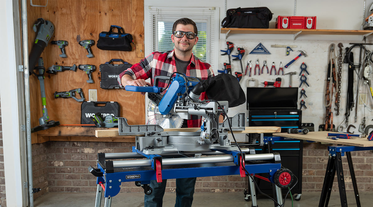 Contractor operating a blue sliding compound miter saw in a workshop with tools, clamps, and lumber visible