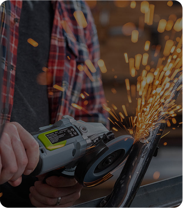 Angle grinder cutting a metal pipe, producing bright orange sparks beside a person wearing a plaid shirt