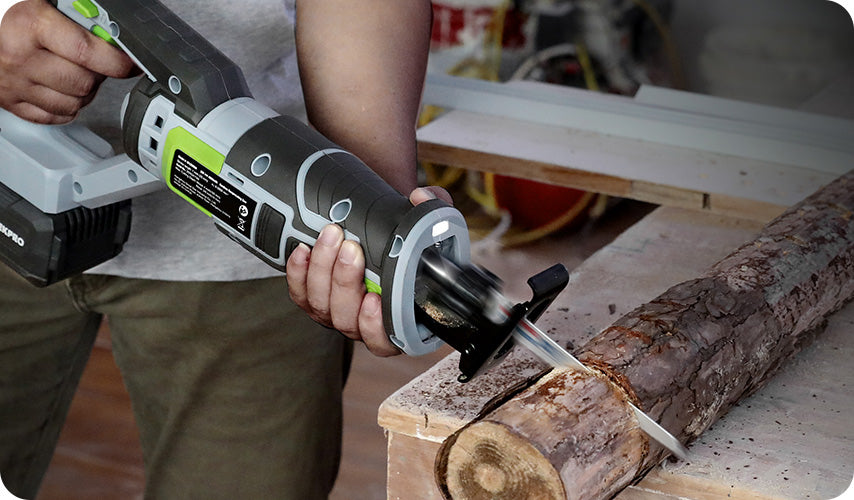 Cordless reciprocating saw cutting a rough log on a wooden workbench with a visible metal blade