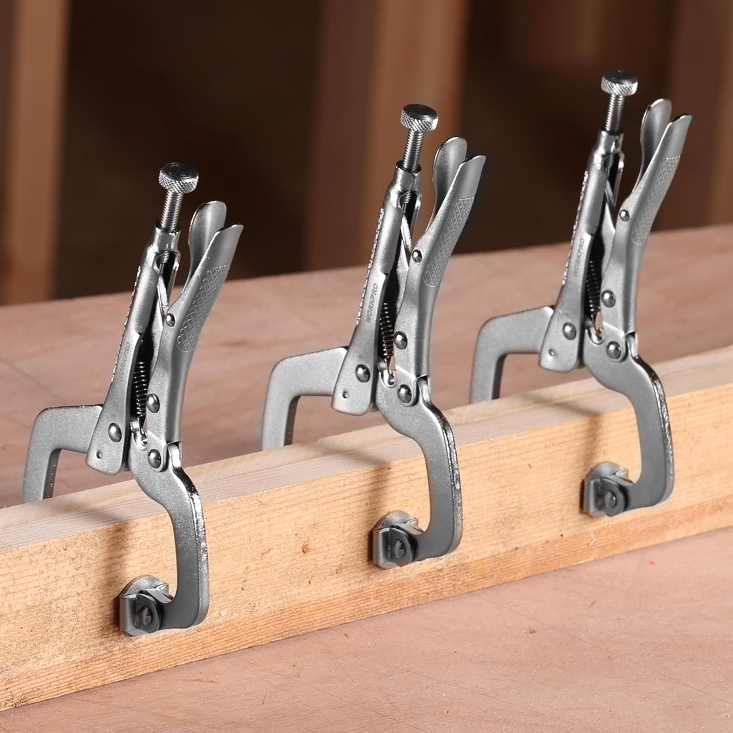 Set of three swivel-pad C-clamps standing on a wooden surface, gray steel locking jaws
