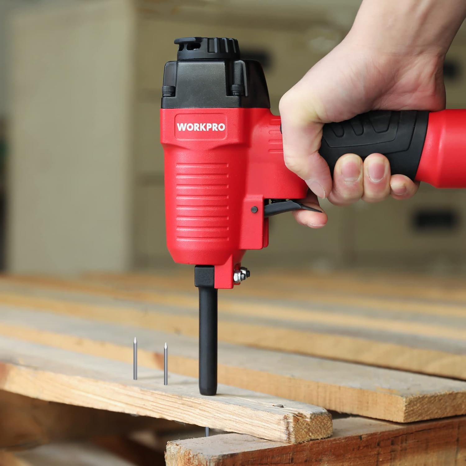 Pneumatic nail remover with red body and black handle, hand holding tool on wood