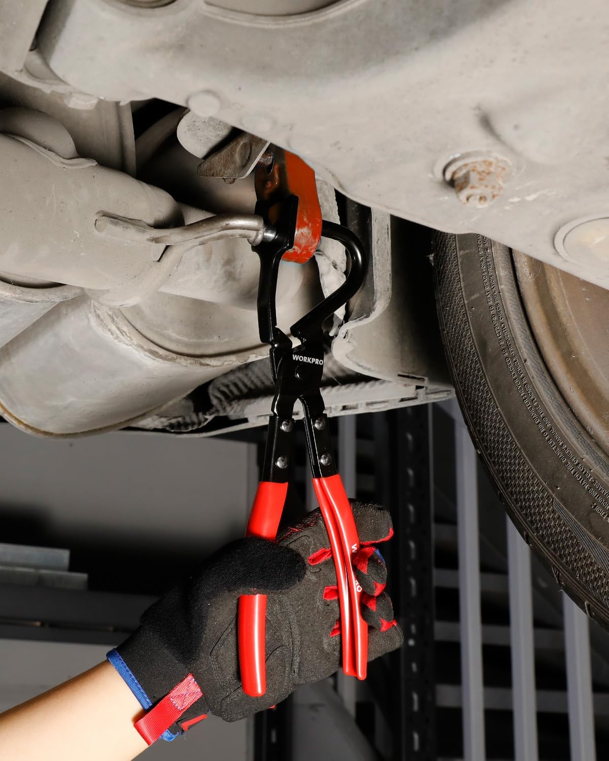 Red-handled exhaust hanger removal pliers attached to a vehicle exhaust hanger