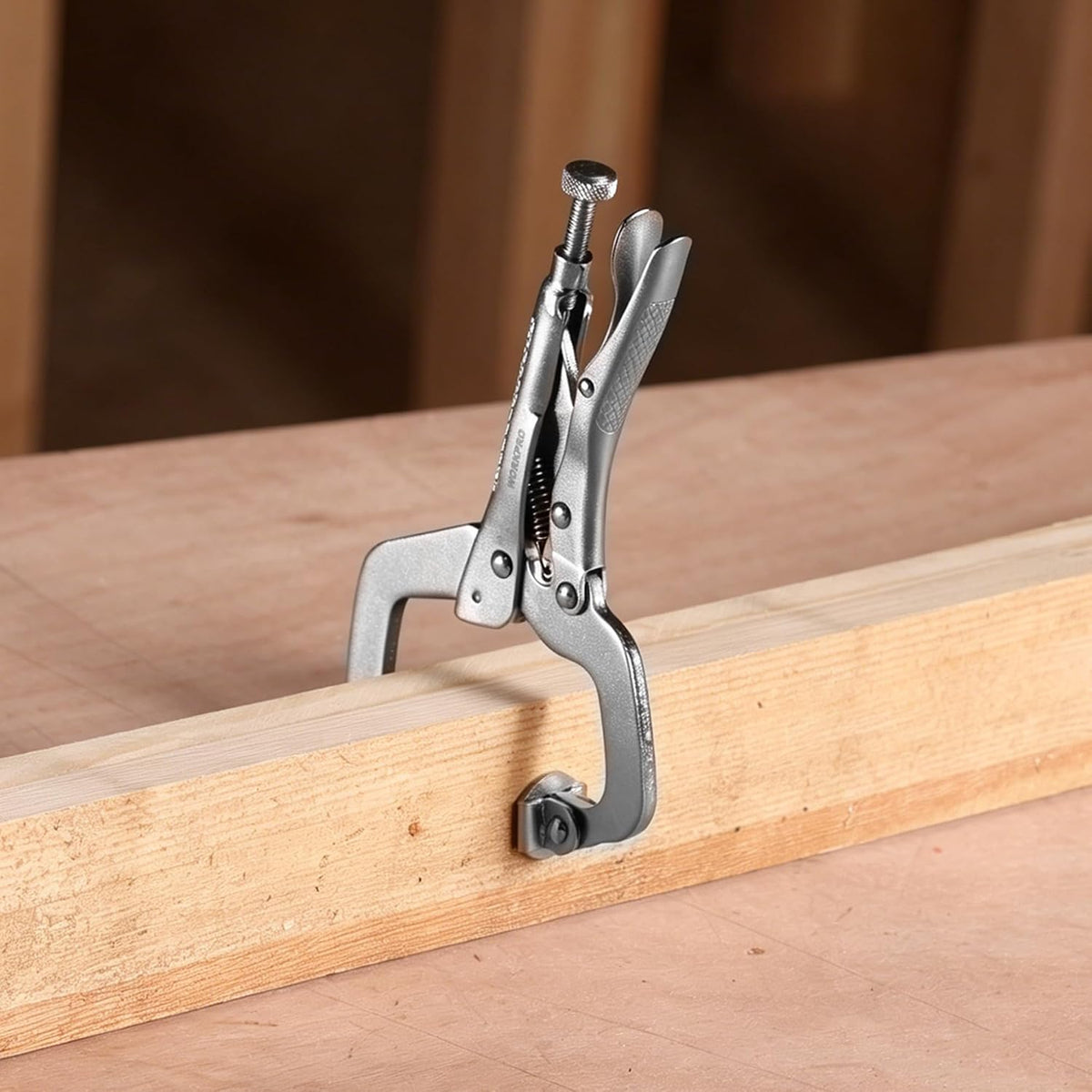 Locking C-clamp with swivel pad pressed on a wooden beam, chrome-silver finish
