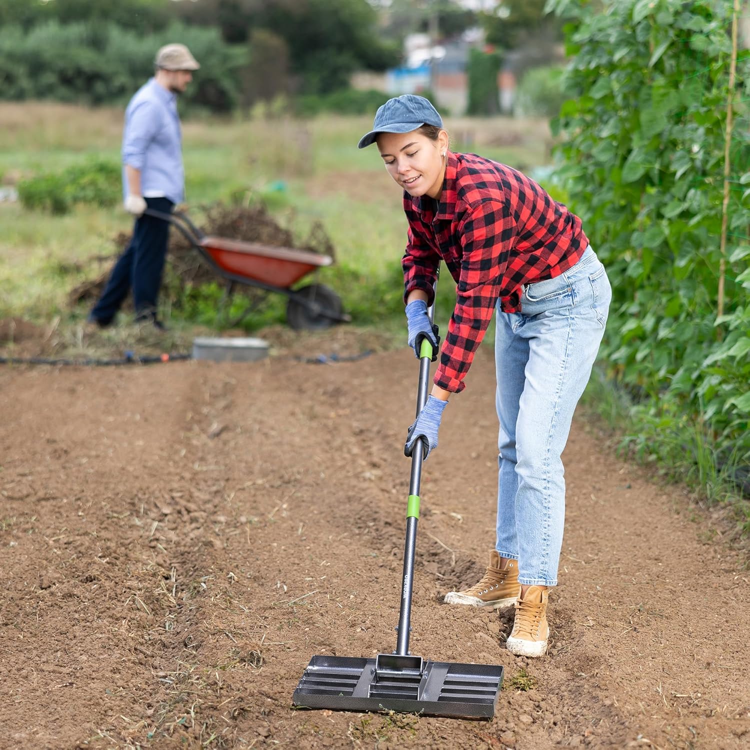 Lawn leveling rake with green grip and metal leveling head on dirt path