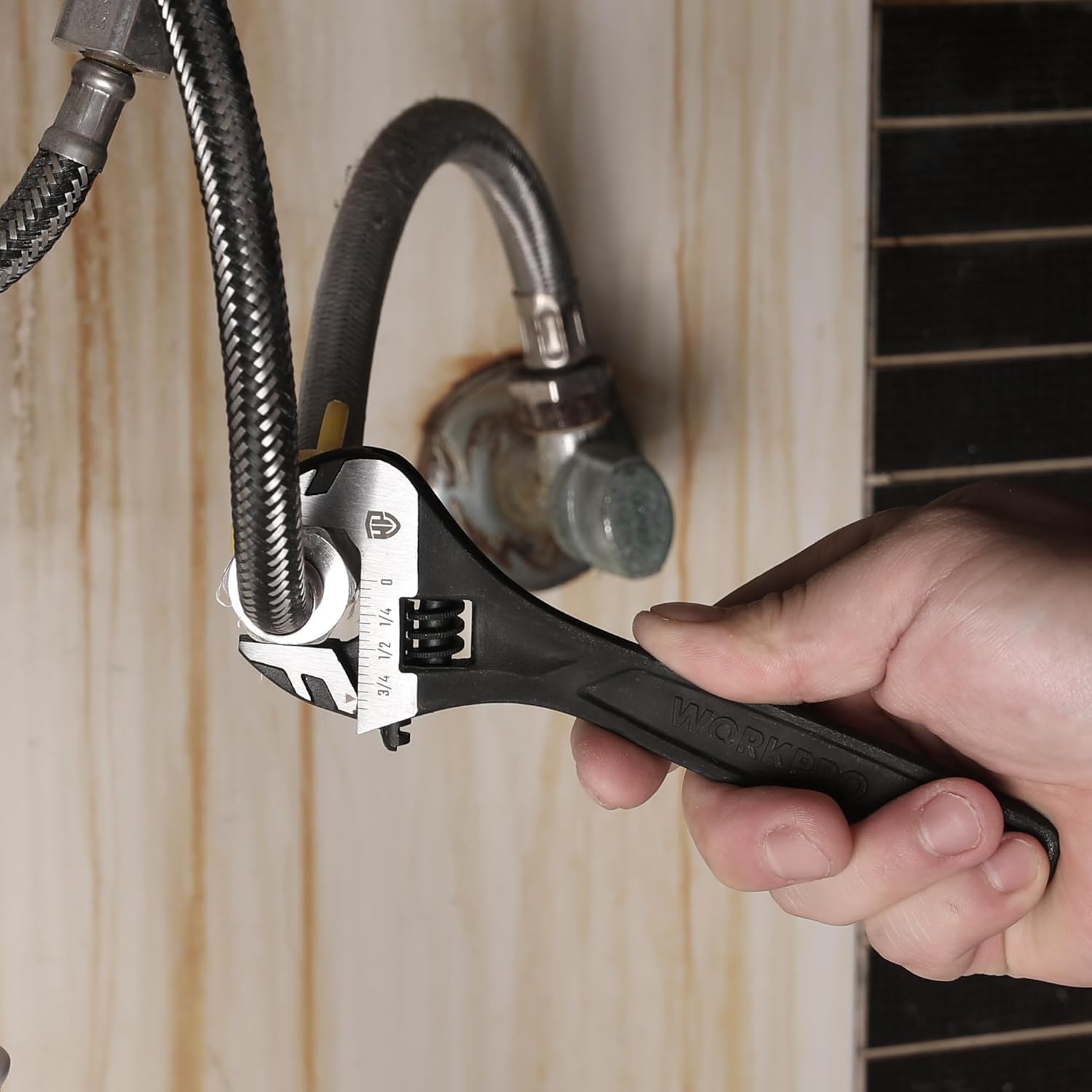 Black adjustable wrench gripping a metal pipe fitting in a hand.