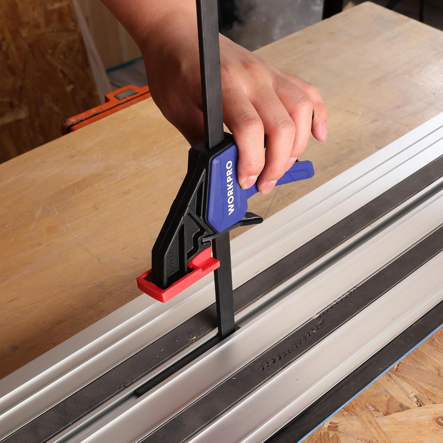 Quick-release track saw clamp on a guide rail with blue handle and red release tab.