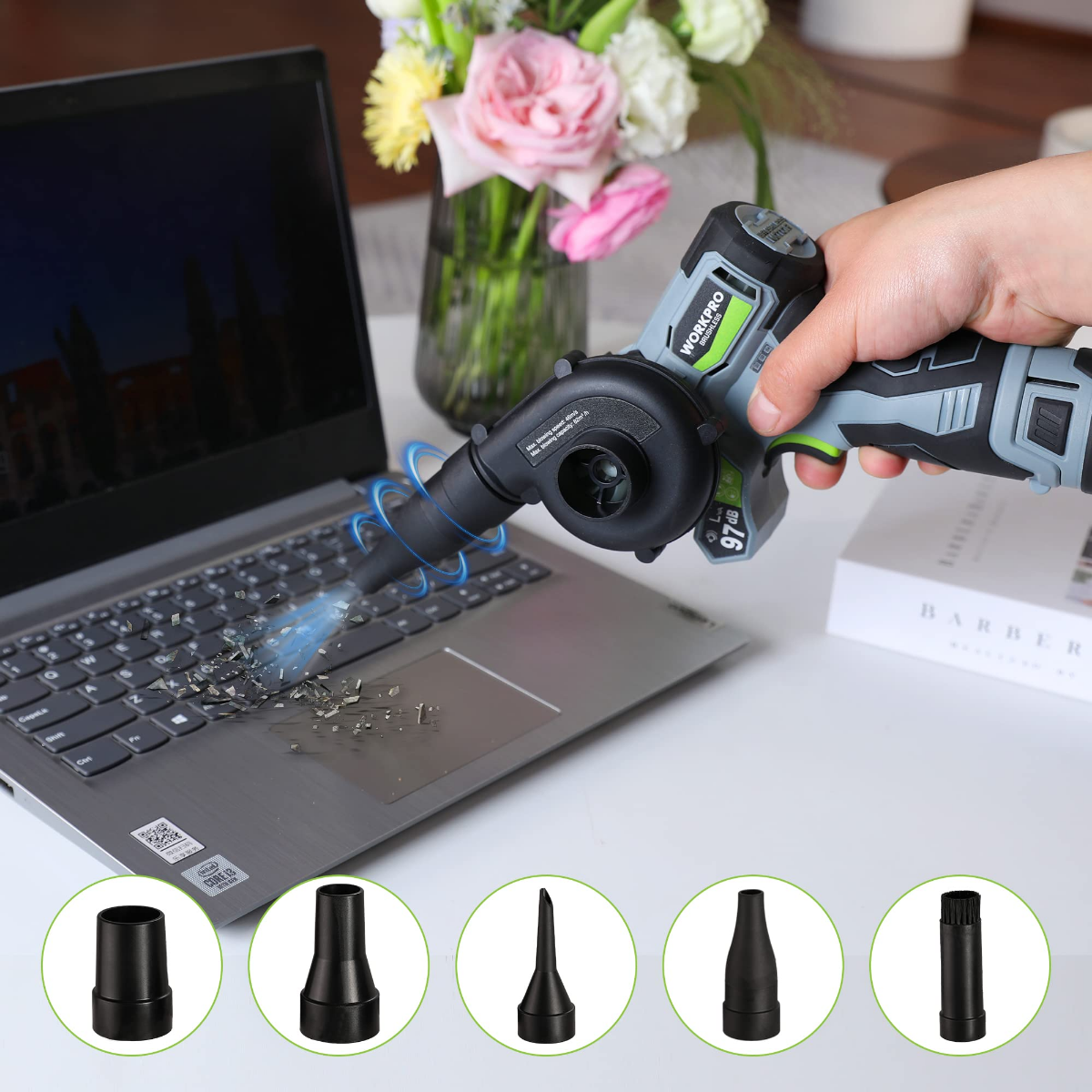 Cordless electric blower nozzle blowing dust near a laptop keyboard; green-accent grip
