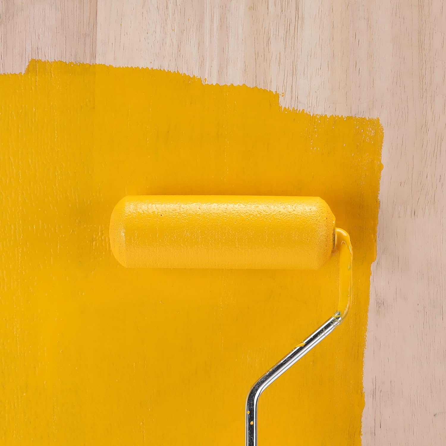 Yellow mini foam paint roller applying paint on a wall, smooth covered roller surface