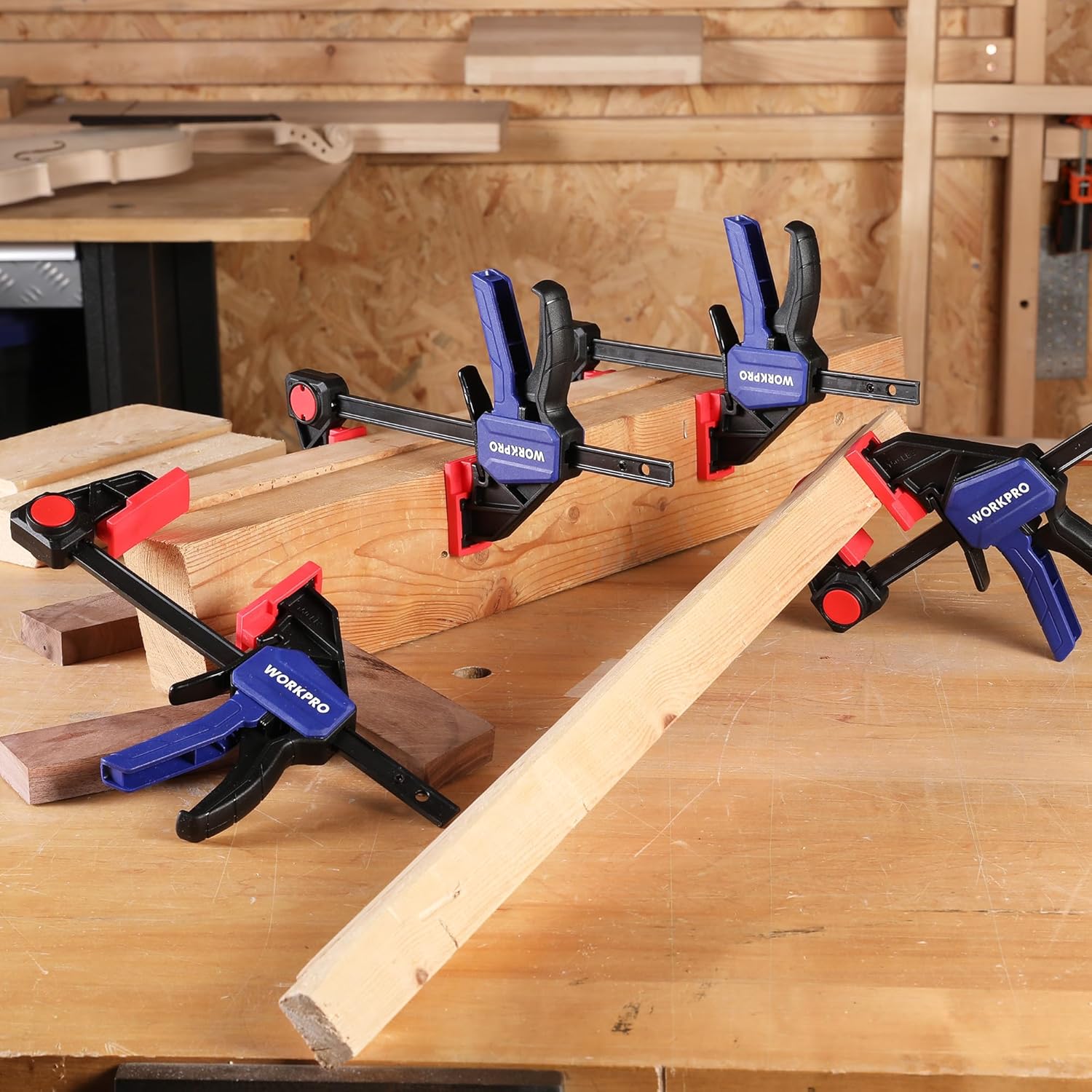 Multiple bar clamps securing wood boards in a workshop, red pads and blue trigger handles