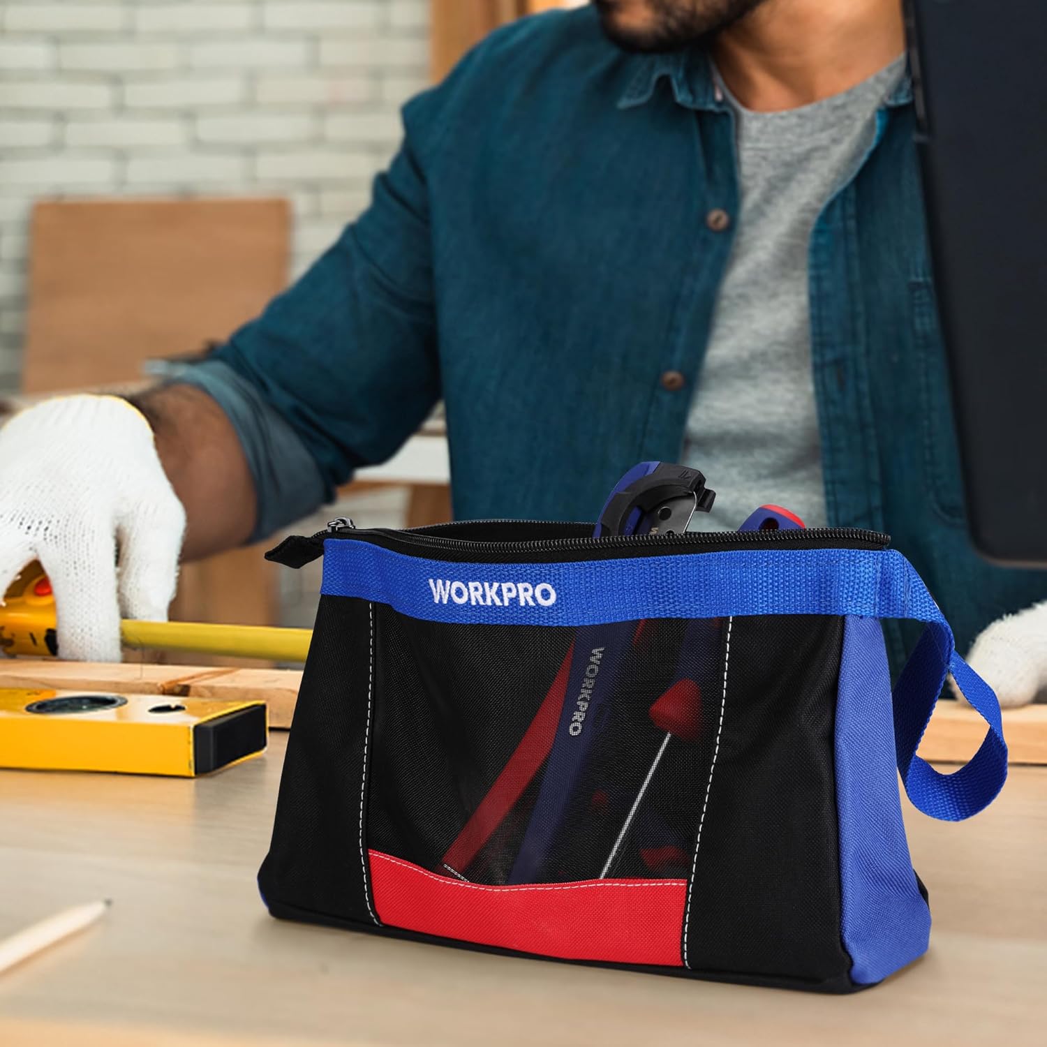 Black-and-blue zipper tool pouch with red front panel, carried on a workbench