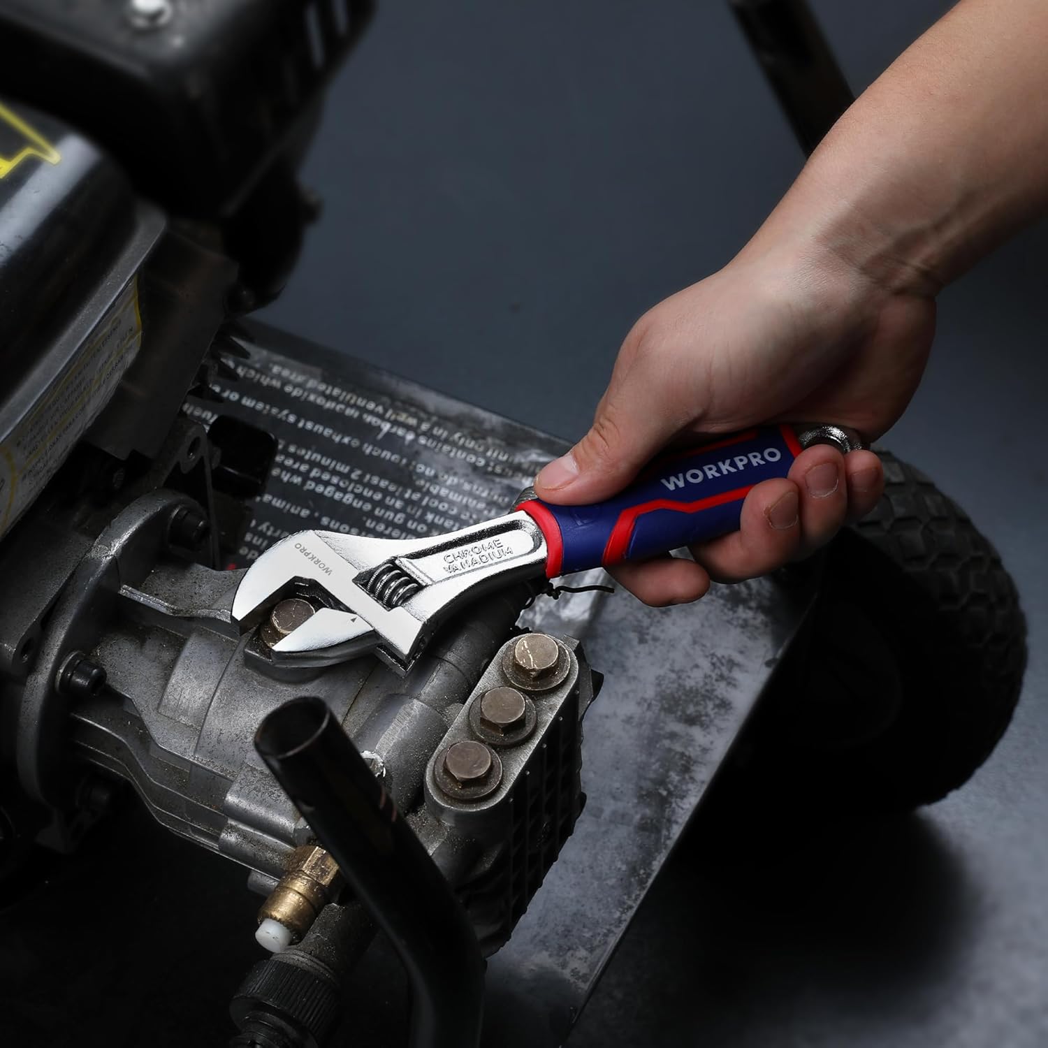 Adjustable wrench in use on a vehicle engine component, blue/red TPR grip visible
