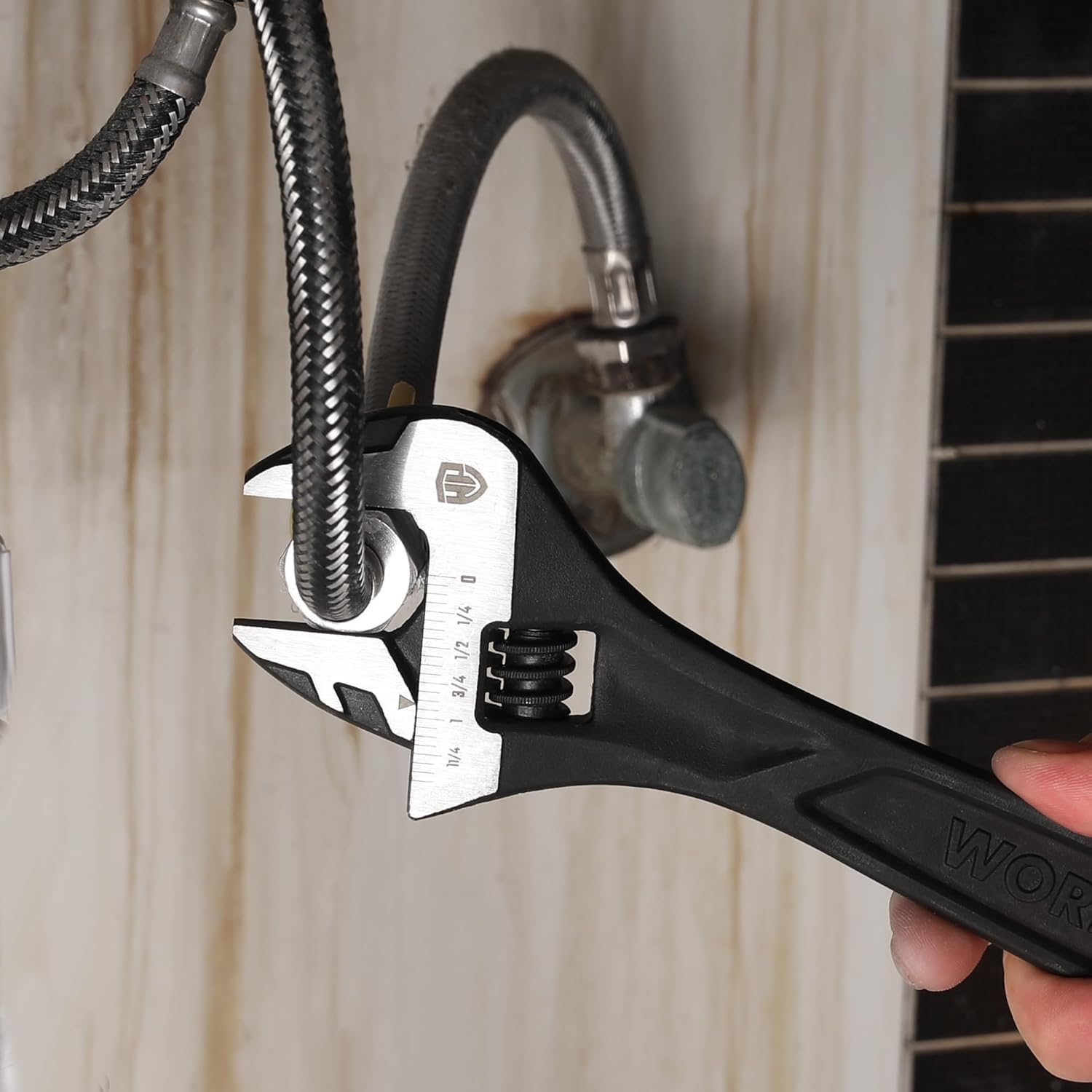 Handheld black adjustable wrench gripping a metal pipe fitting