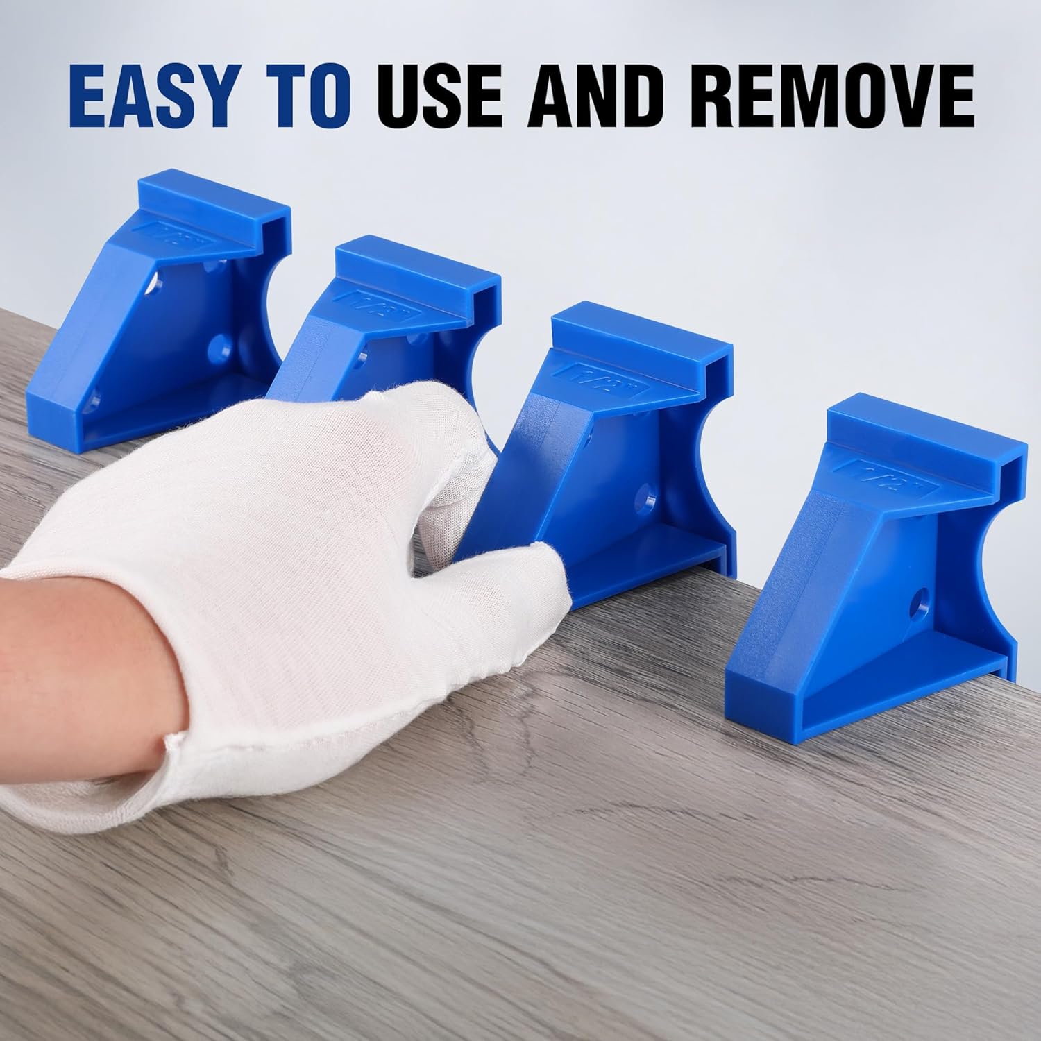 Blue triangular floor spacers being removed by a gloved hand from laminate planks