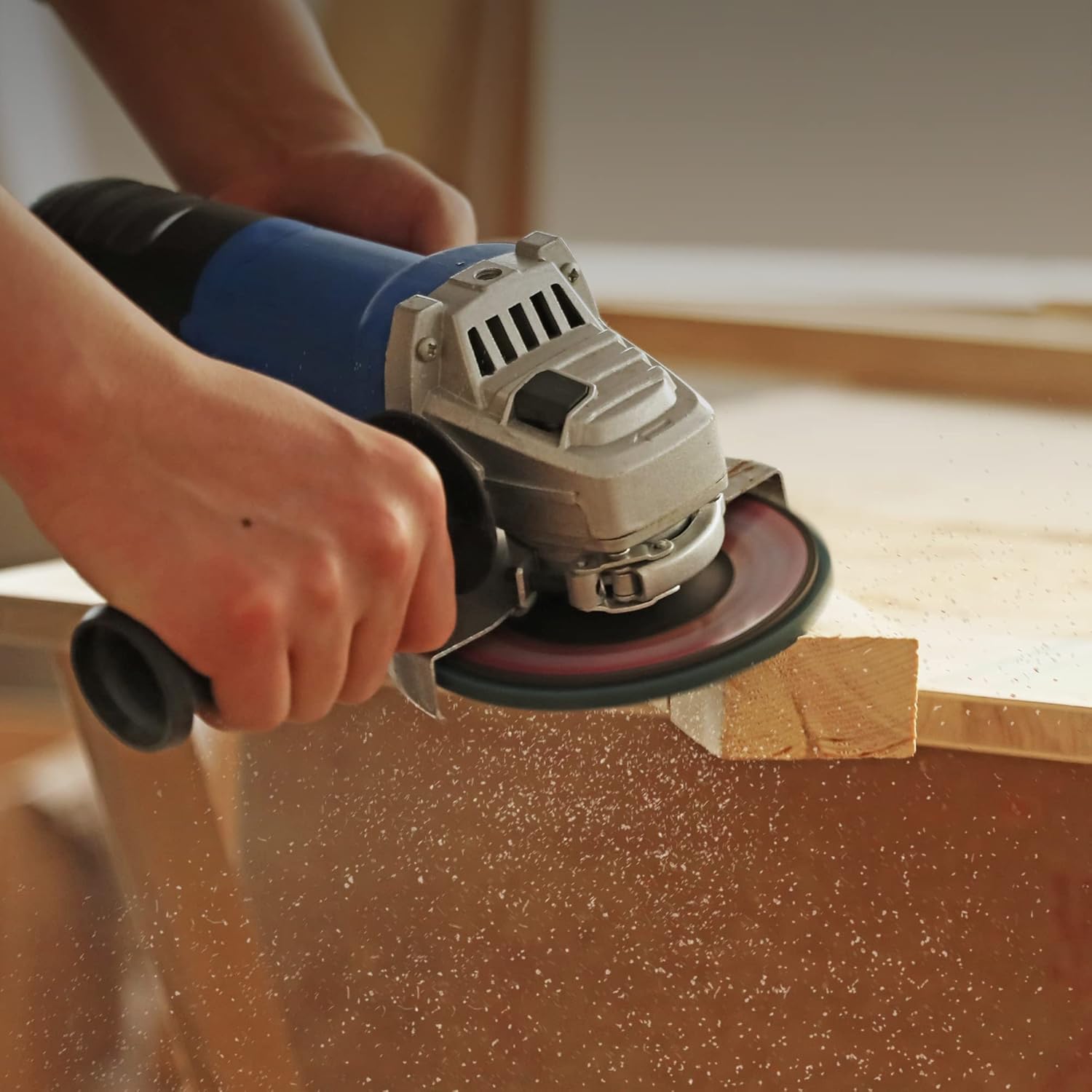 Hand using an angle grinder with a blue flap sanding disc on wood