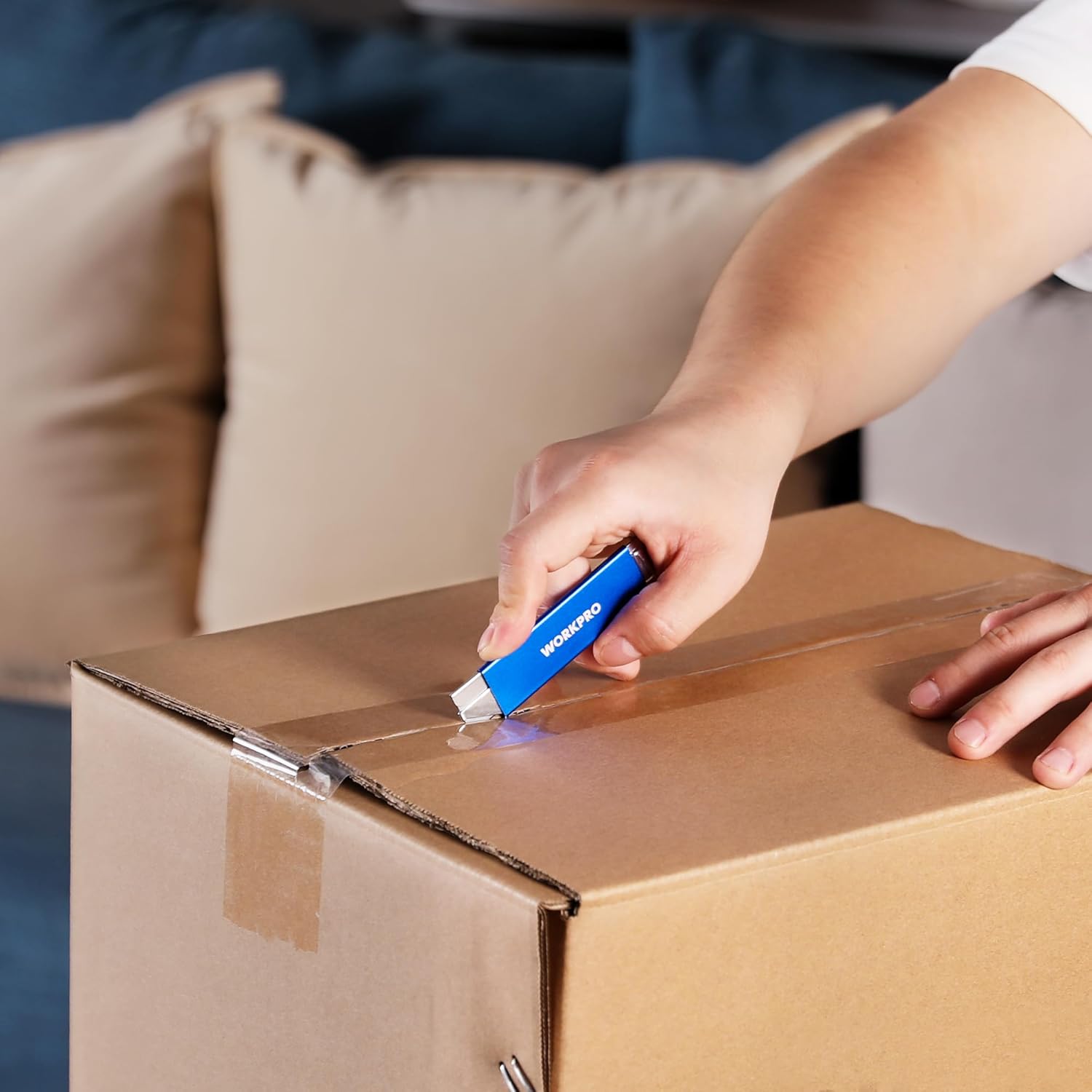 Hand using blue retractable box cutter to cut a cardboard shipping box