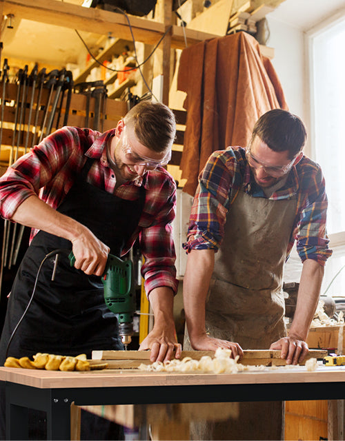Two people working at a woodworking bench, drilling and shaping wood in a workshop with warm light