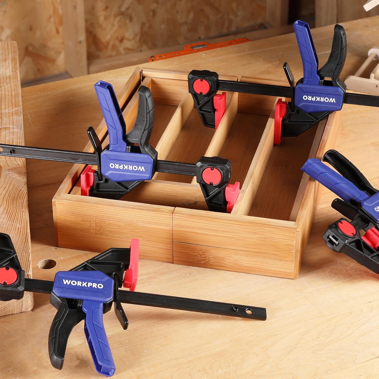 Four 6-inch bar clamps gripping wooden box interior with red pads and blue trigger handles