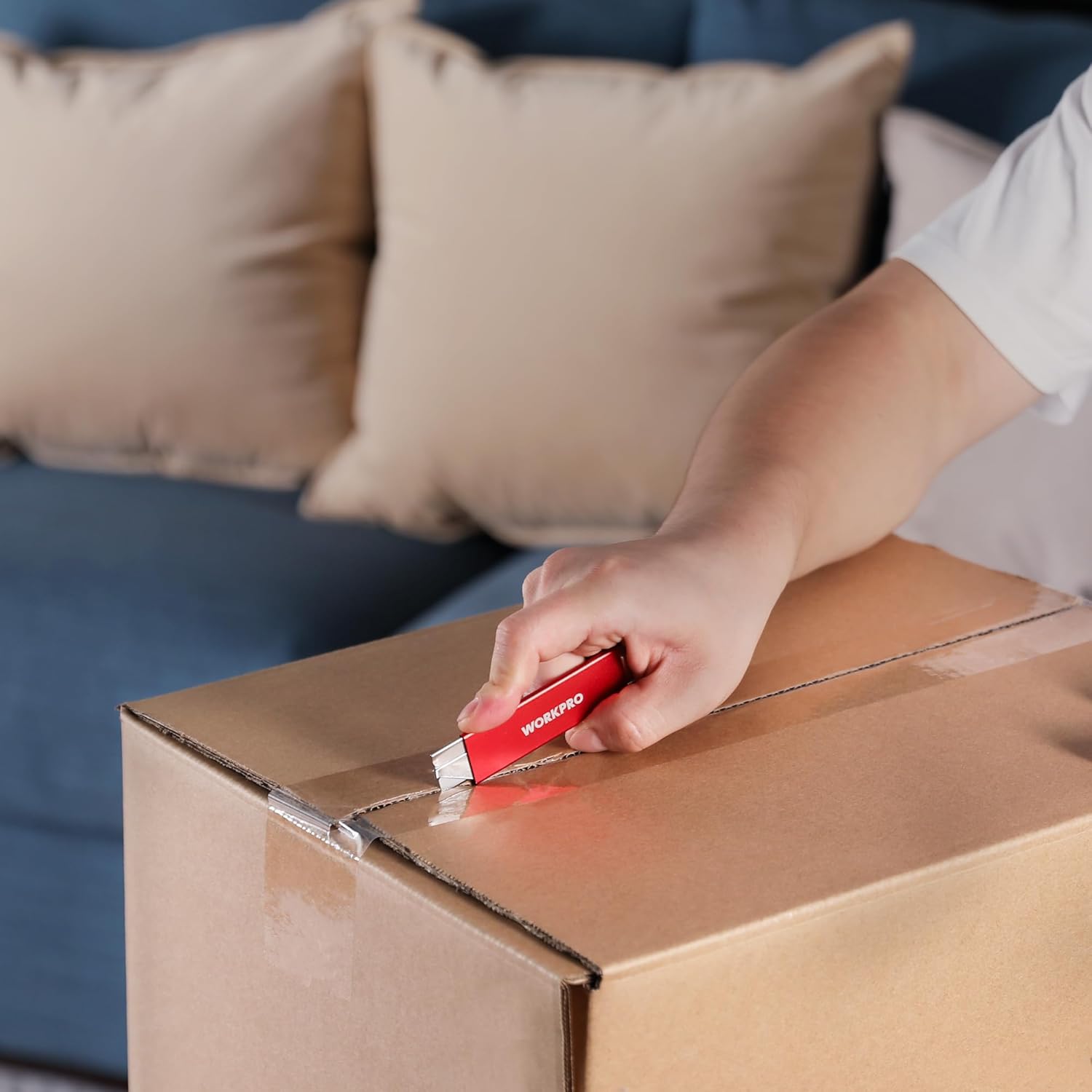 Hand using red retractable utility knife to cut cardboard box seam