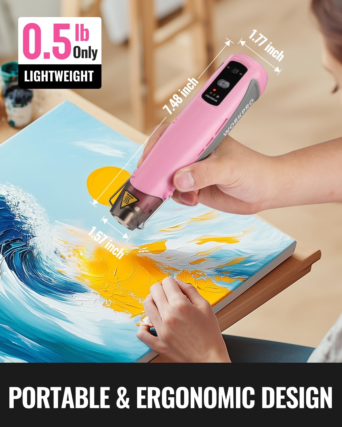 Pink mini cordless heat gun in hand over artwork; lightweight portable design