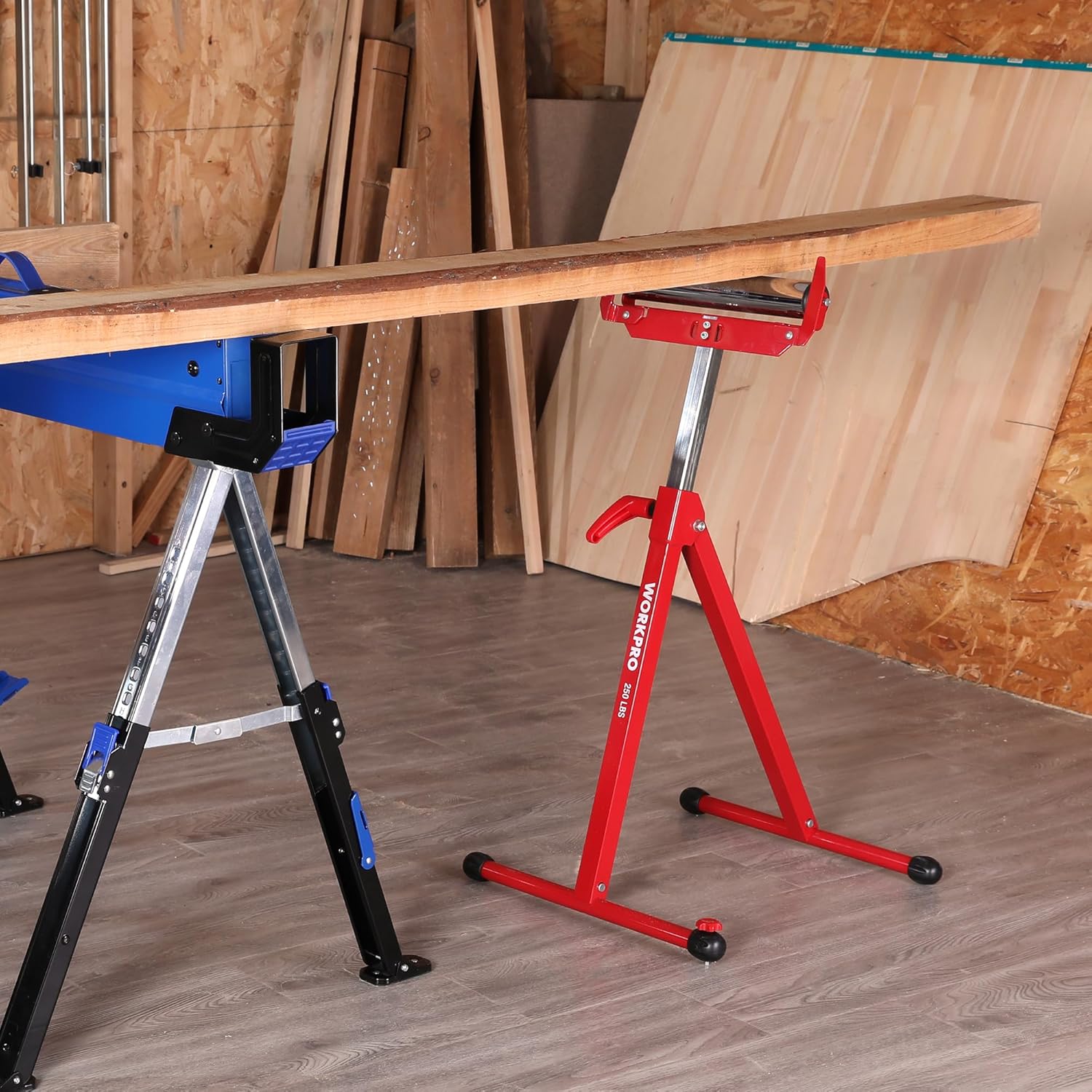 Red folding roller stand supporting a long wooden board in a workshop