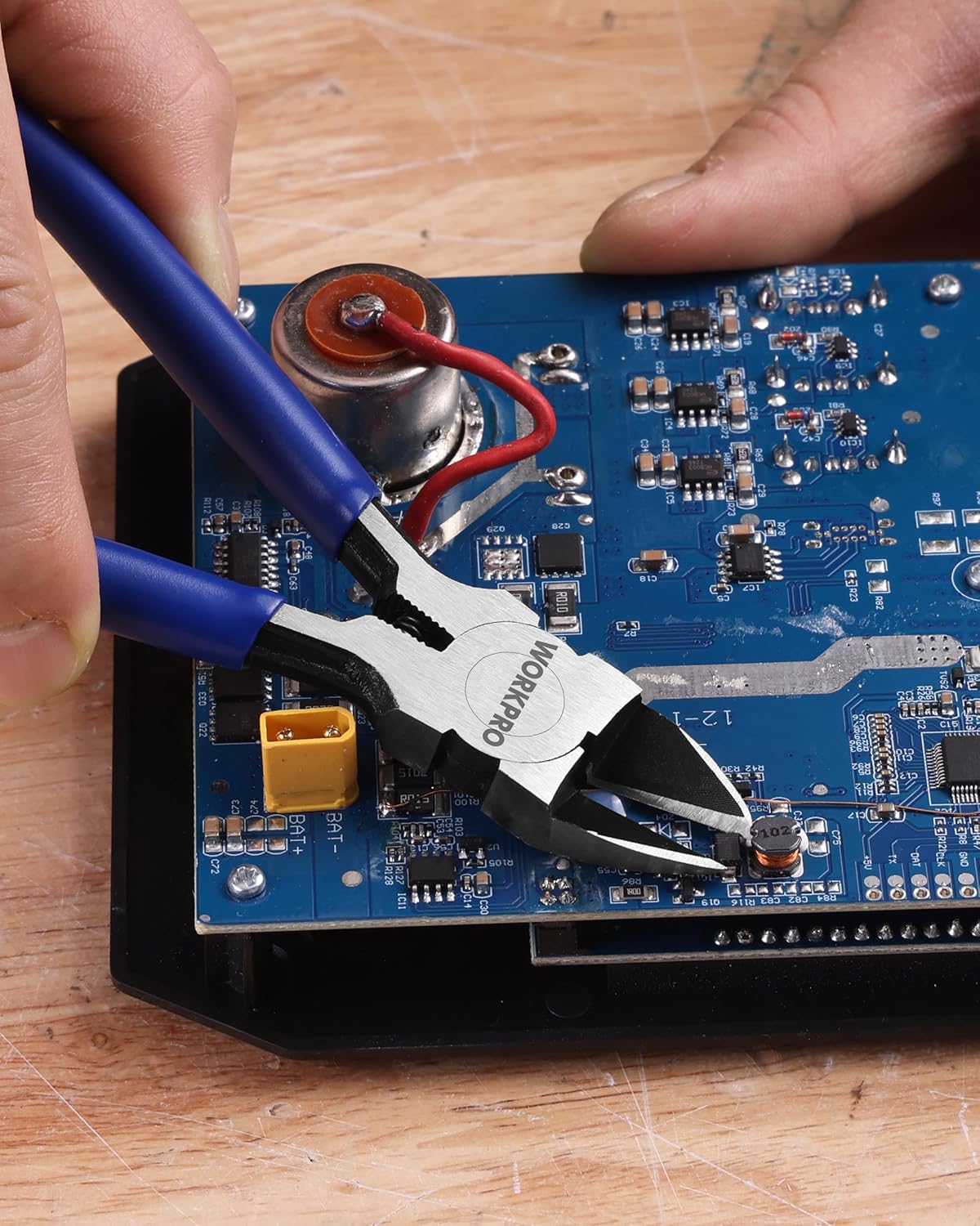 Flush cutter with blue handles snipping a red wire near a circuit board