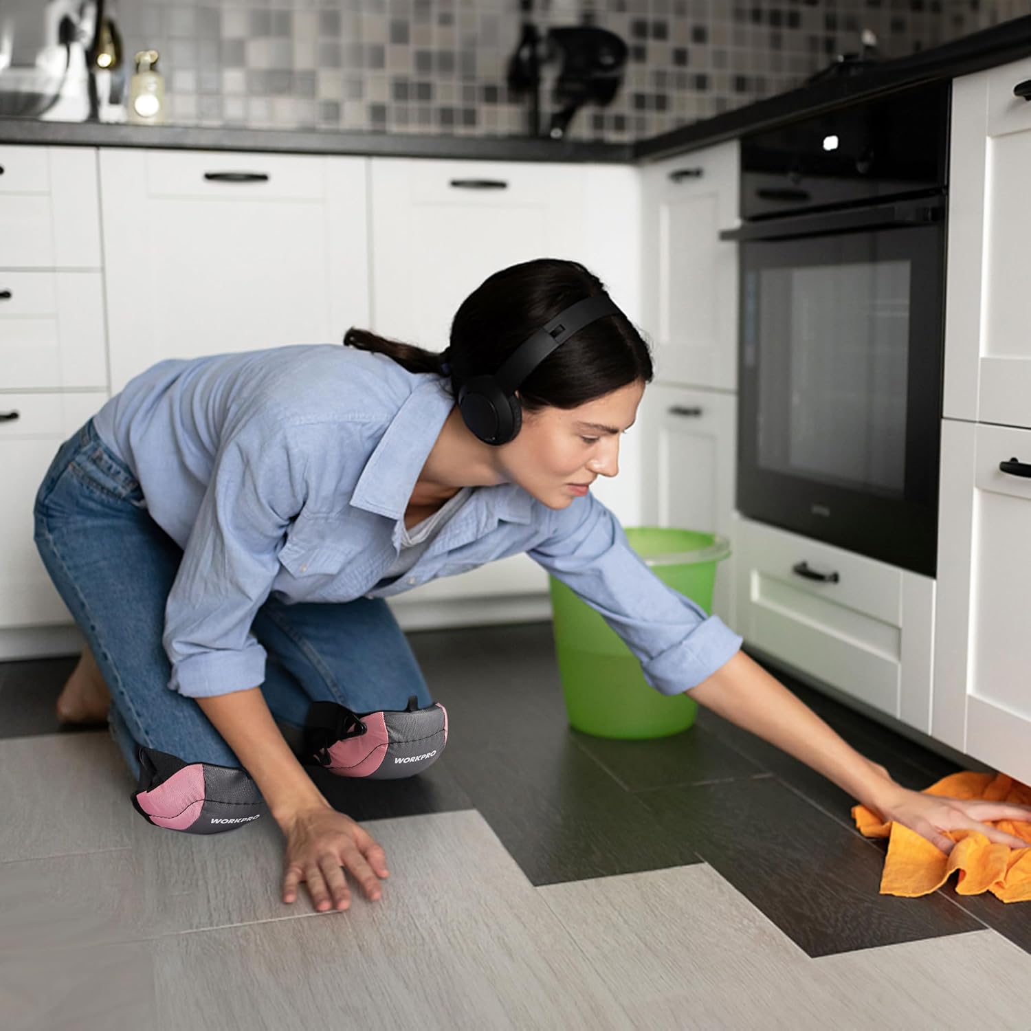 Pink knee pad with black strap in use on tile floor, worn while kneeling.