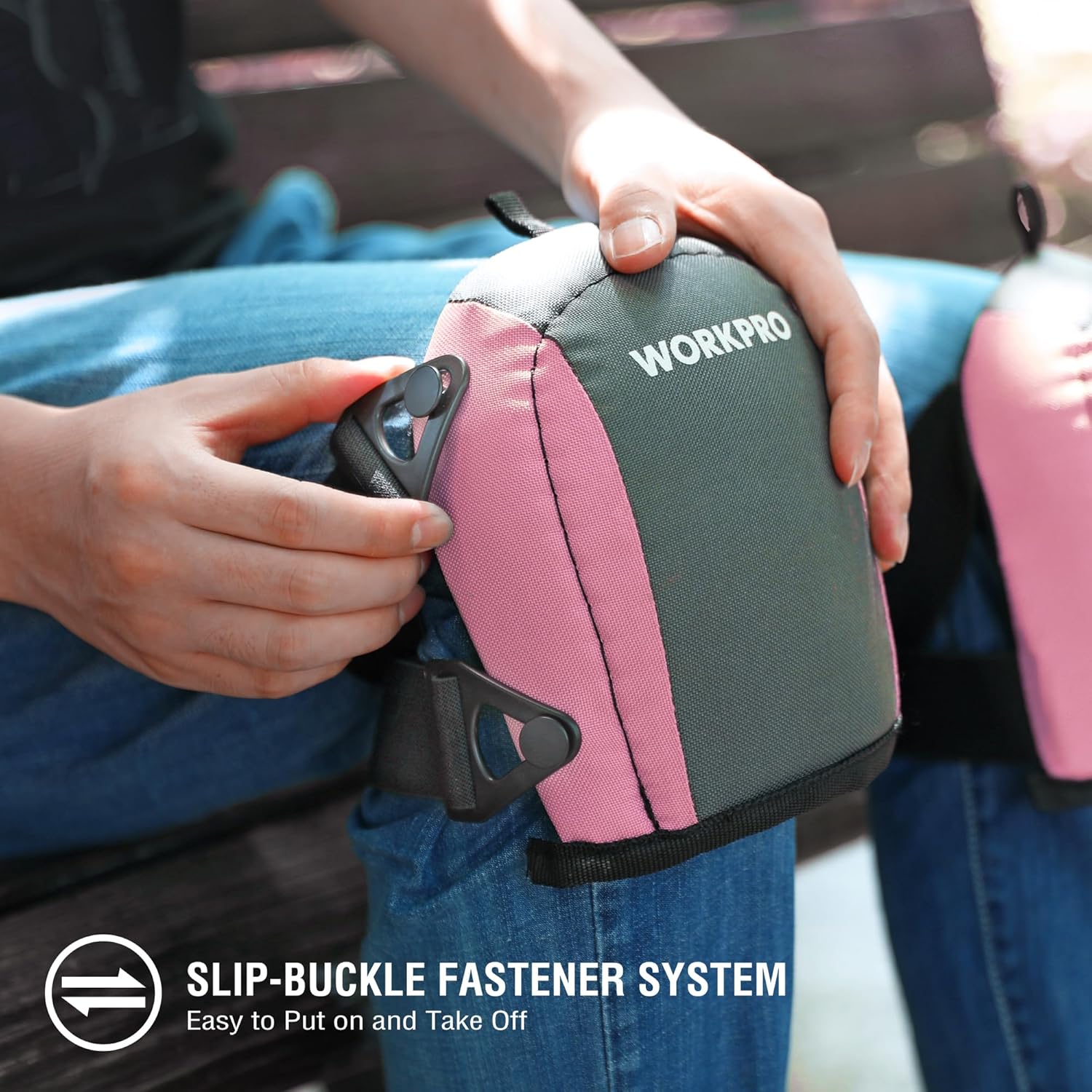 Pink and gray knee pad with black strap and buckles, held for fastening.