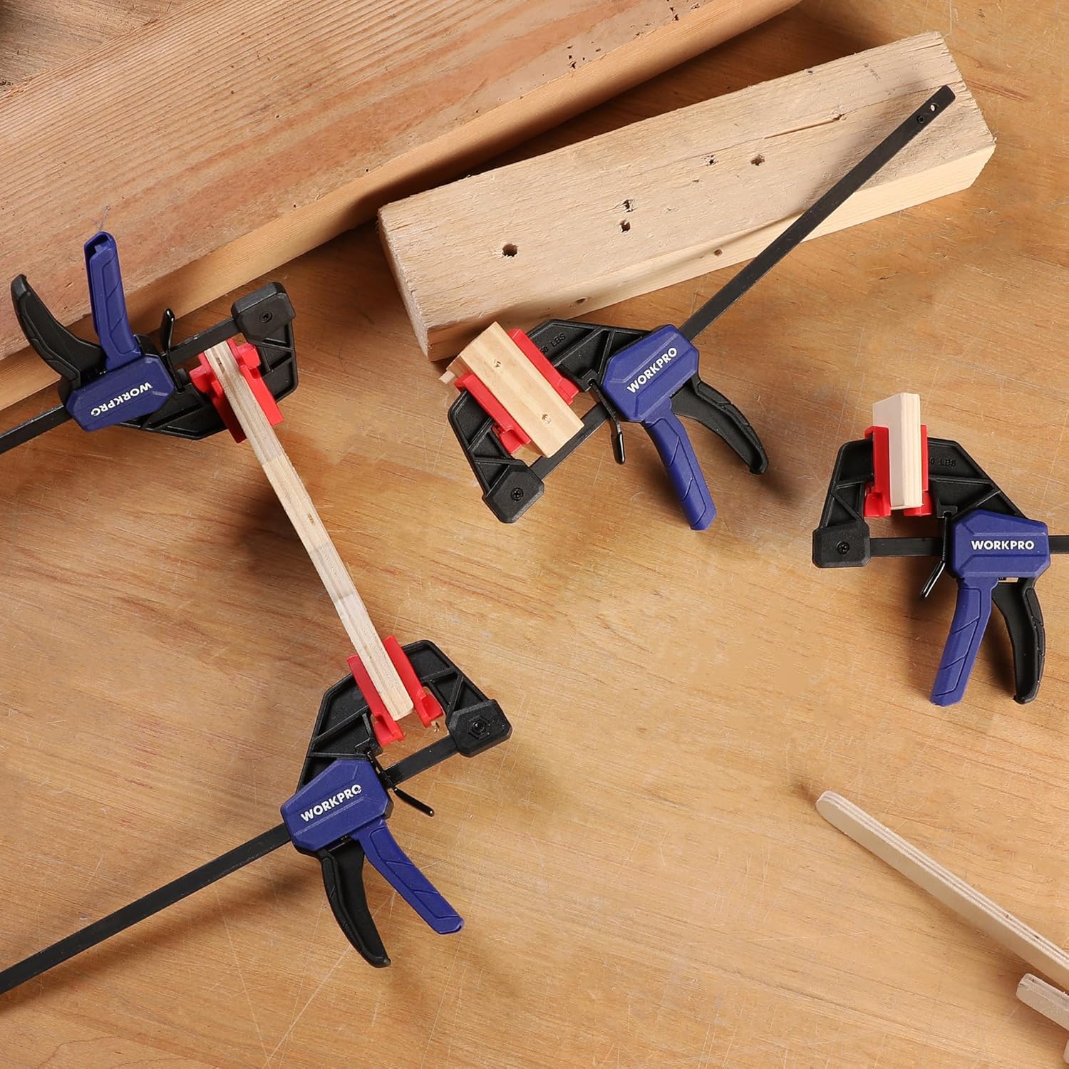 Four mini bar clamps securing stacked wood panels, black frames with blue handles