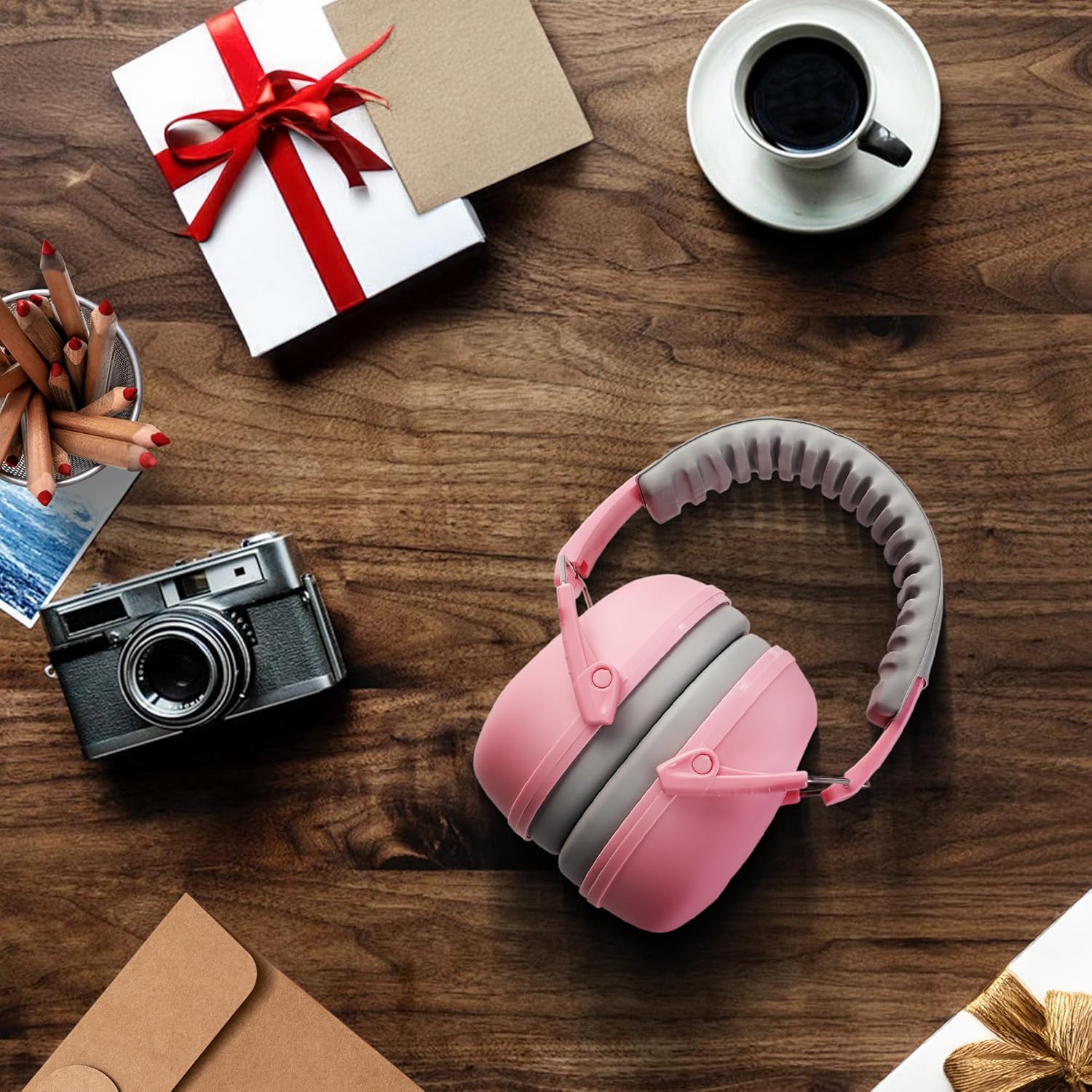 Pink and gray kids ear defenders with padded ear cushions, resting on a surface.