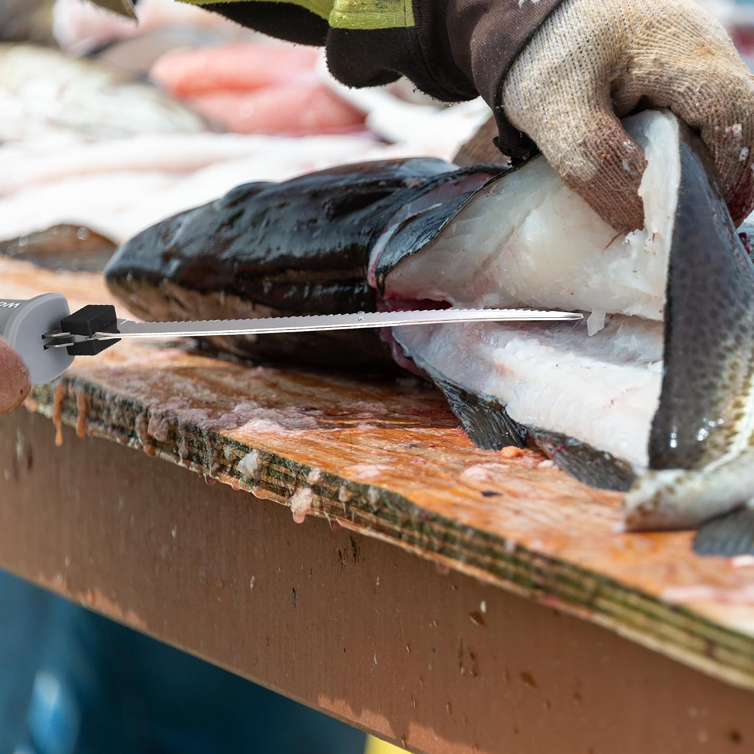 Serrated blade separating fish fillets on a wooden board.