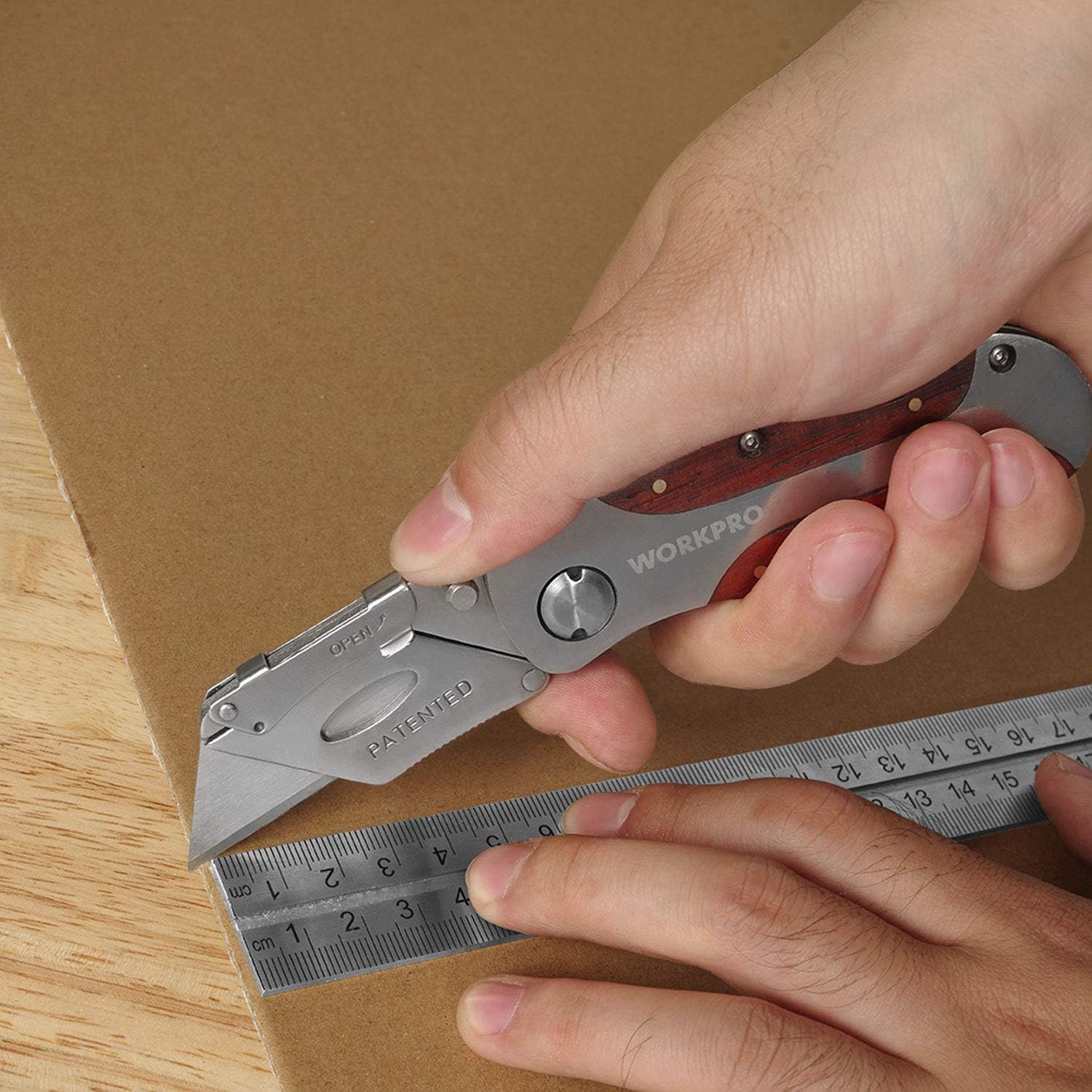 Person gripping a folding utility knife with red wood-grain handle against a wooden board