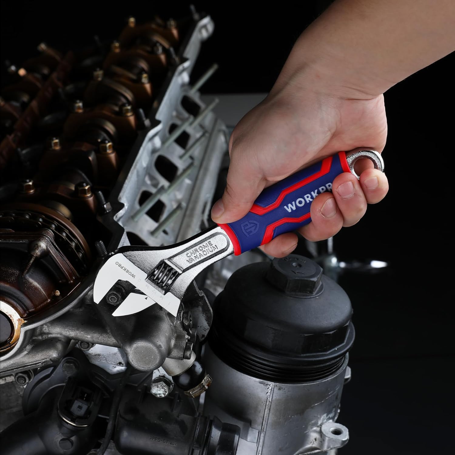 Adjustable wrench held over an engine bay component, blue/red anti-slip grip visible