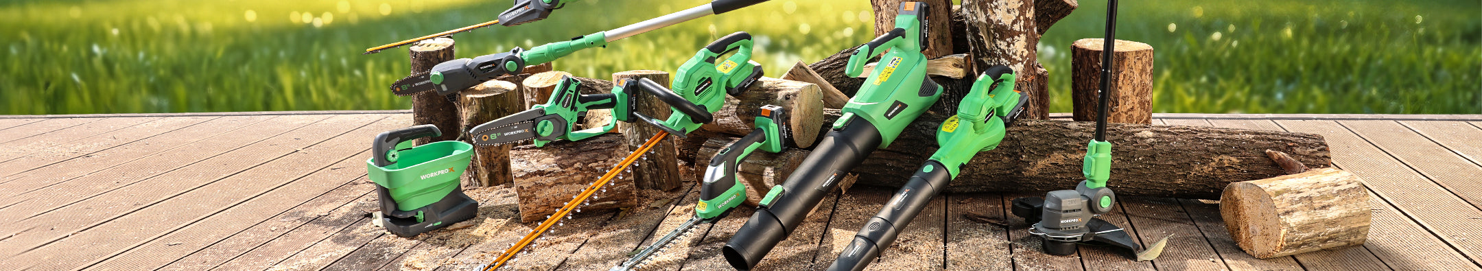 Green power tools and batteries on a wooden deck, with logs and yard tools in an outdoor yard