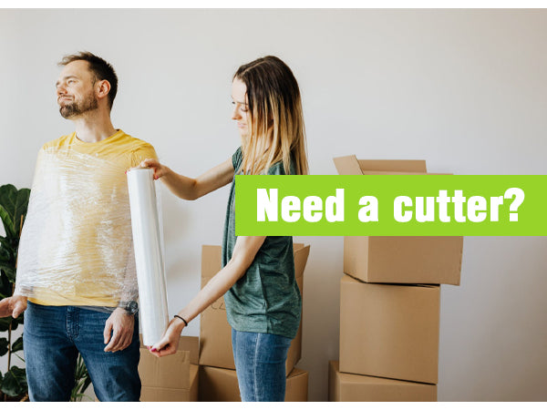 Safety box cutter with retractable blade, held in hand near cardboard boxes