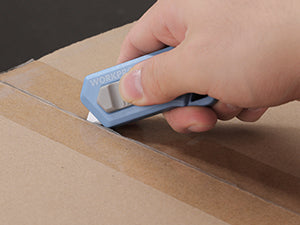 Hand using ceramic safety box cutter to score cardboard along an edge