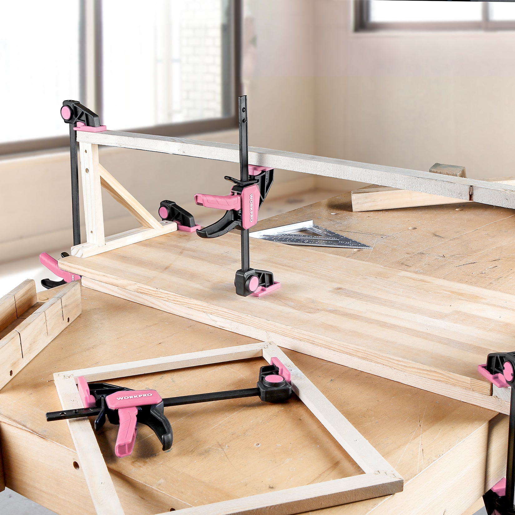 Pink bar clamp set securing plywood and boards on a workbench for woodworking
