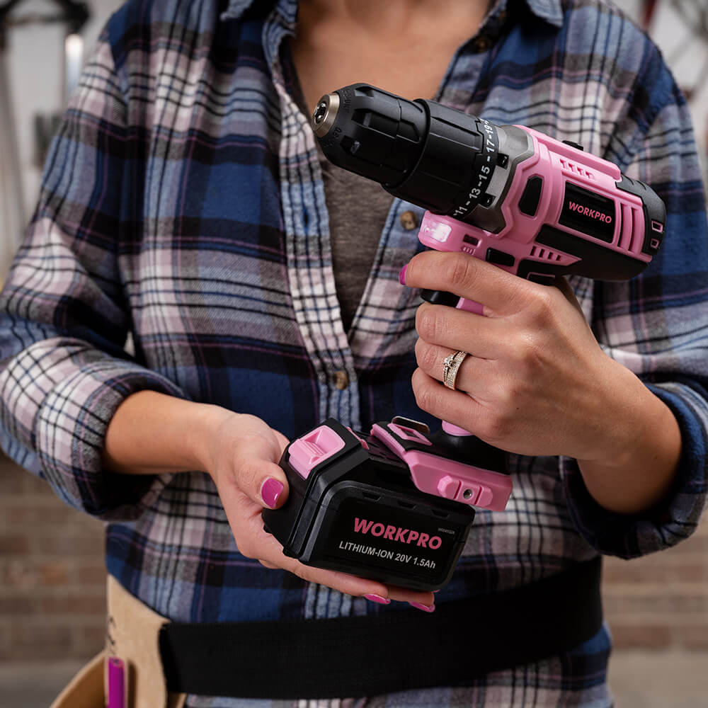 Hand holding a pink and black cordless drill, innovation and quality focus in a workshop setting