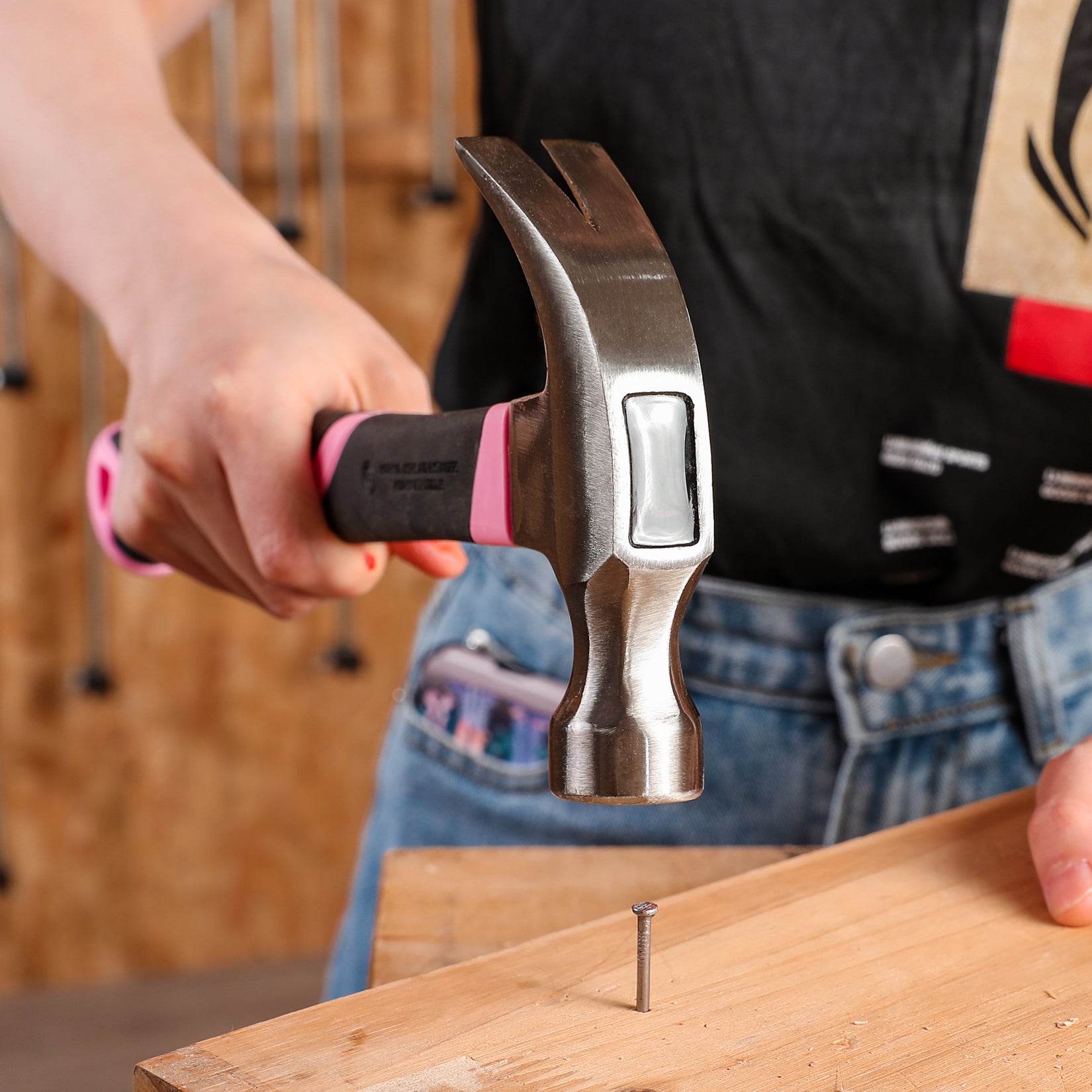 Claw hammer with steel claws gripping a nail on a wooden board, held in hand