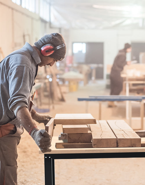 Worker in a workshop handling wooden boards with innovation and quality, wearing gloves and a face shield
