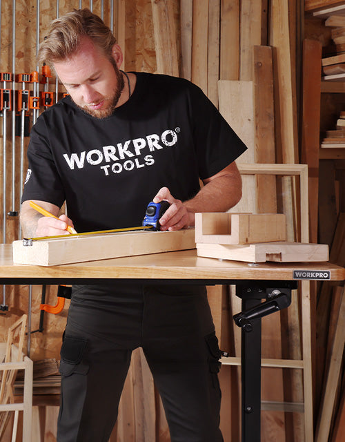 A carpenter in a workshop cutting wood with a tool, wearing WORKPRO tools shirt, showing innovation and quality