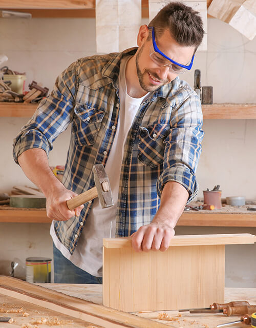 Carpenter with safety glasses and a hammer installing a wooden cabinet, showing innovation and durable quality