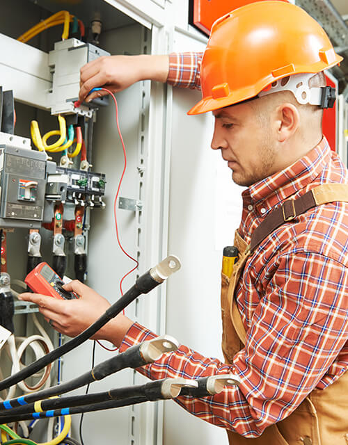 Electrician in an orange hard hat working on a control panel, innovation and quality shown in secure wiring
