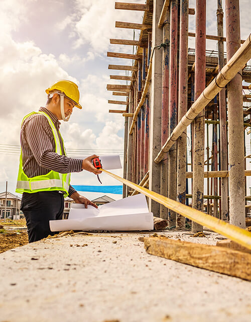Construction worker in a yellow hard hat checking plans near steel rebar, innovation and quality on site