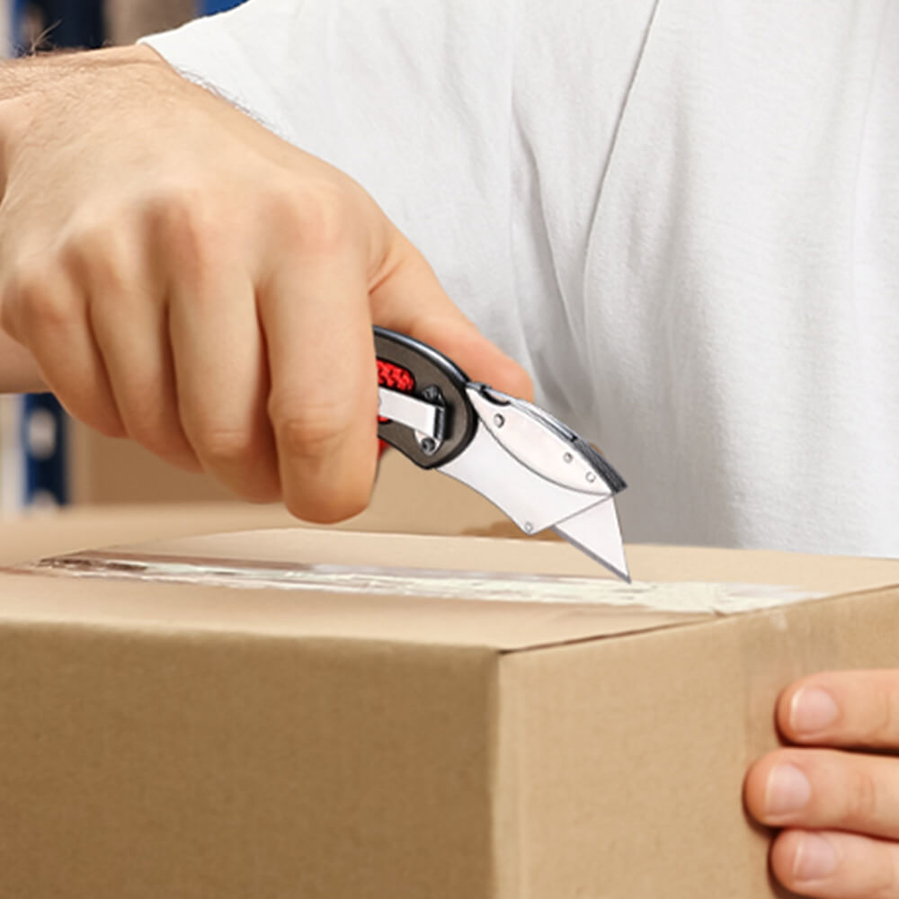 Hand using a folding box cutter on a cardboard package, cutting along the taped seam