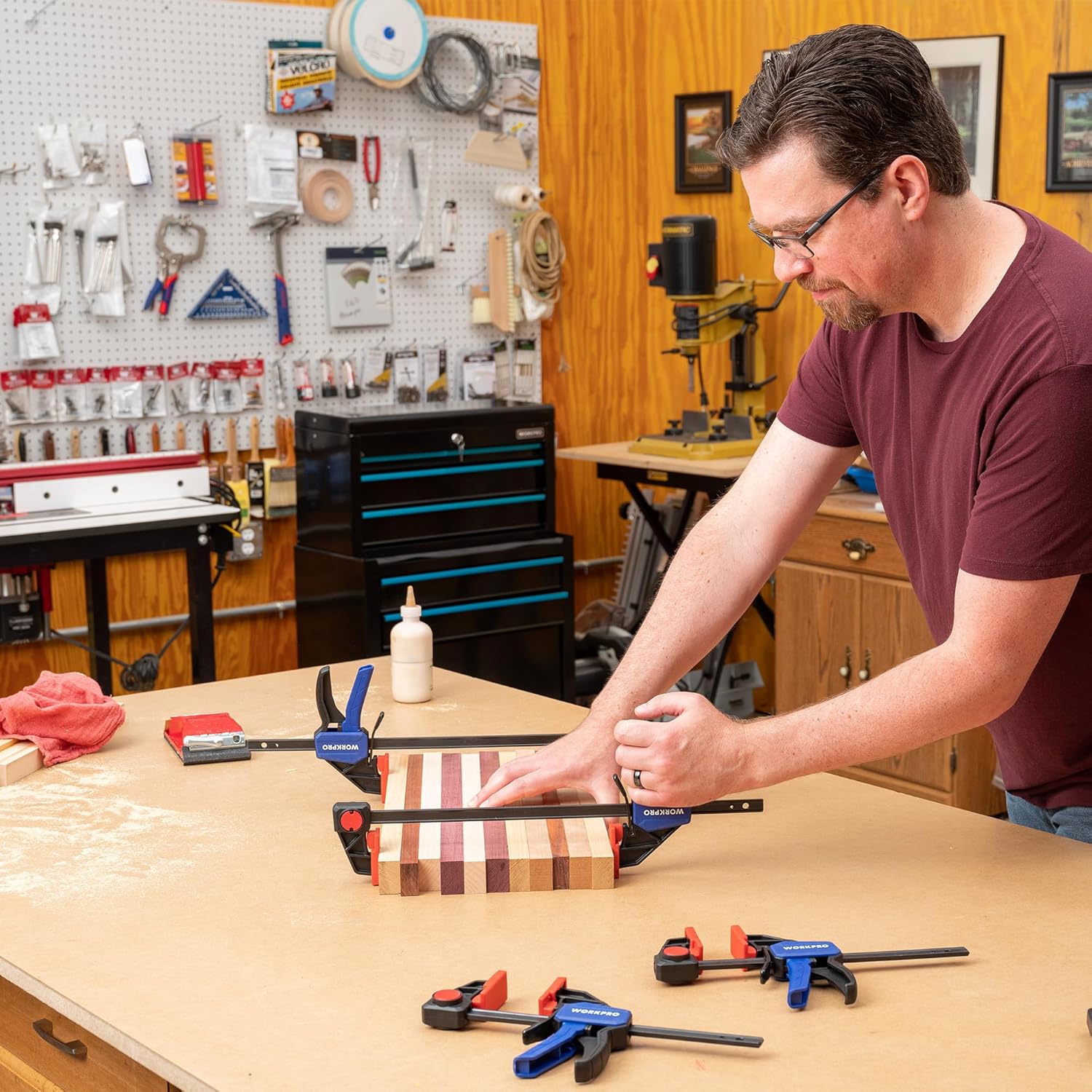 Workshop use of bar clamps on a tabletop for joining wood pieces with red pads and blue triggers