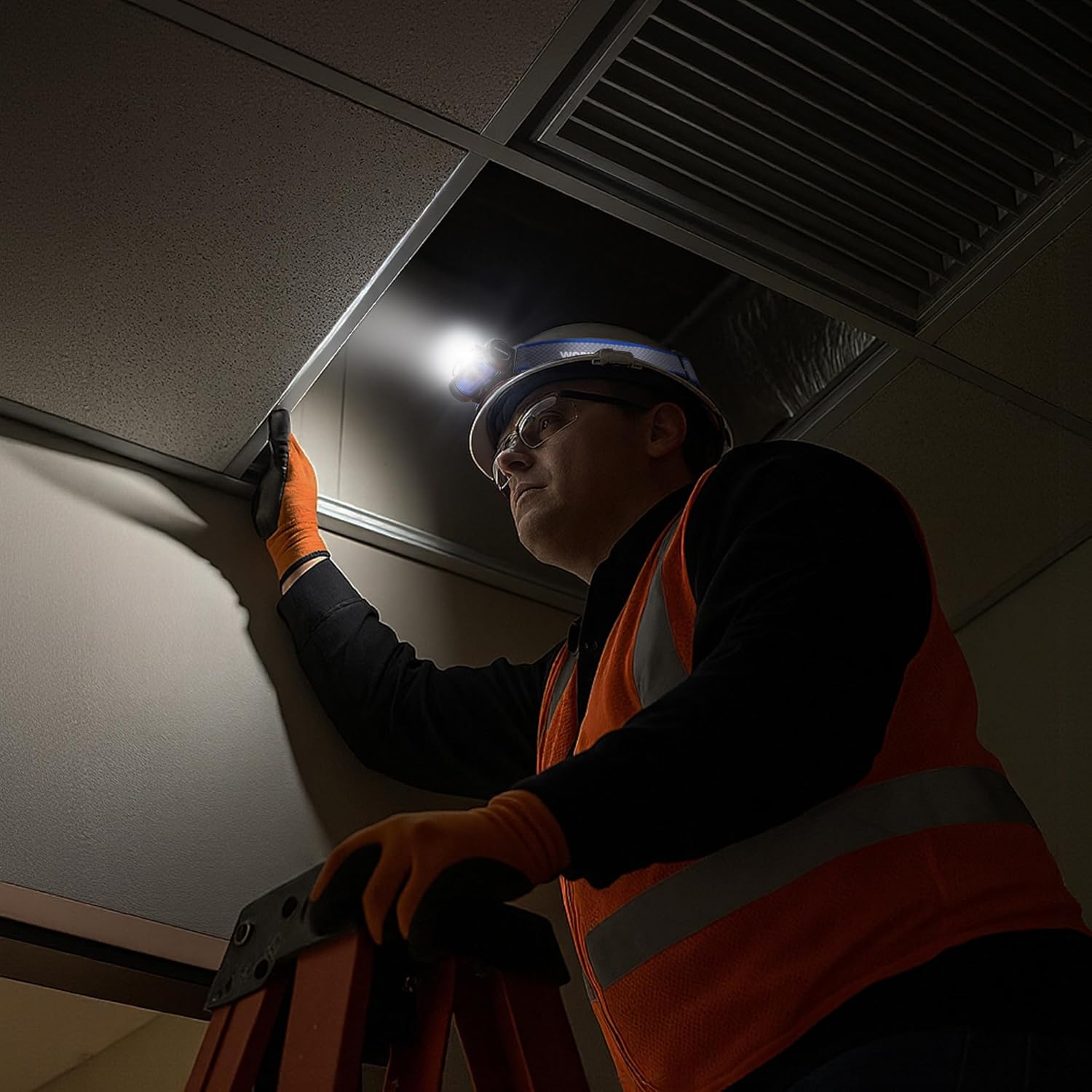 Worker wearing a blue headlamp adjusting overhead ceiling fixture; LED lit